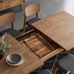 Wooden dining table with a sliding leaf mechanism partially extended in a modern room.