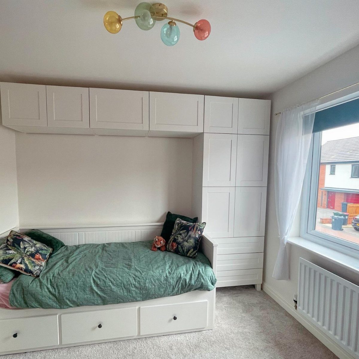 White modular bedroom cabinetry and wardrobe surrounding a bed with green bedding.