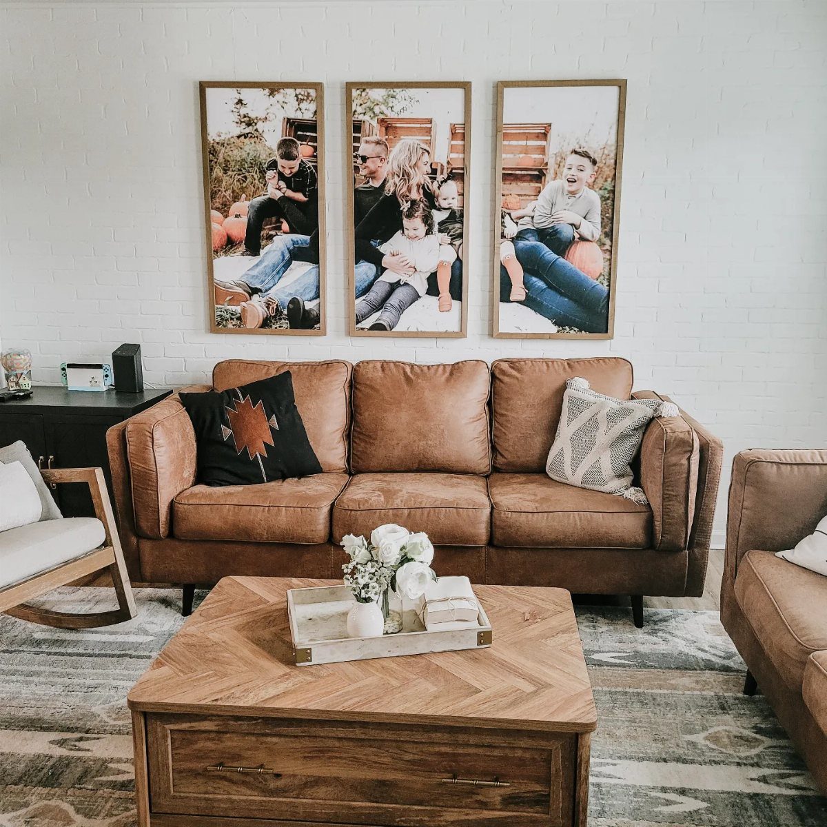 Brown leather sofa and wooden coffee table under three framed family photos on white brick.