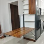 Wooden folding table extended from a grey modular kitchen cabinet in a modern room.