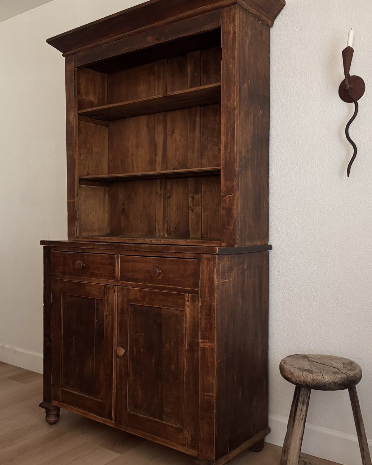 Dark brown wooden hutch with open shelving and lower cabinets against a white wall.