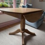 Wooden drop leaf table with one side folded down on a chevron rug.