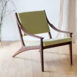 Mid-century modern wood lounge chair with olive green fabric upholstery on wooden flooring.