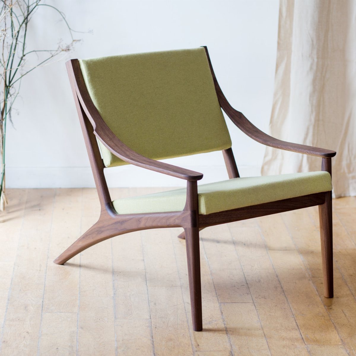 Mid-century modern wood lounge chair with olive green fabric upholstery on wooden flooring.